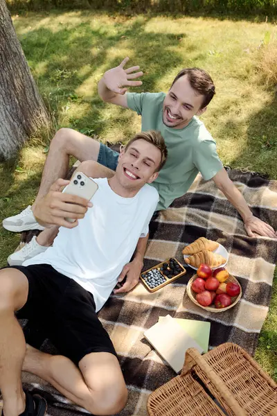 A happy couple captures a joyful selfie while relaxing on a picnic blanket surrounded by nature. — Stock Photo