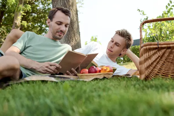A delightful afternoon unfolds as a gay couple shares a picnic, engrossed in reading. — Stock Photo