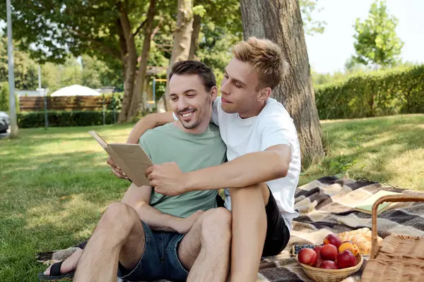 The couple shares an intimate moment, reading together and laughing under a tree on a sunny day. — Stock Photo