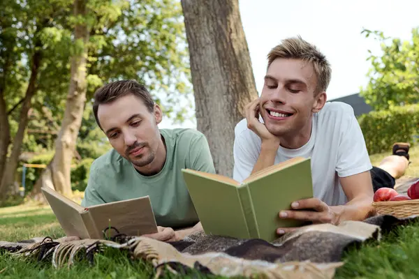 A couple lies on a blanket, absorbed in their books, surrounded by lush greenery and sunshine. — Stock Photo