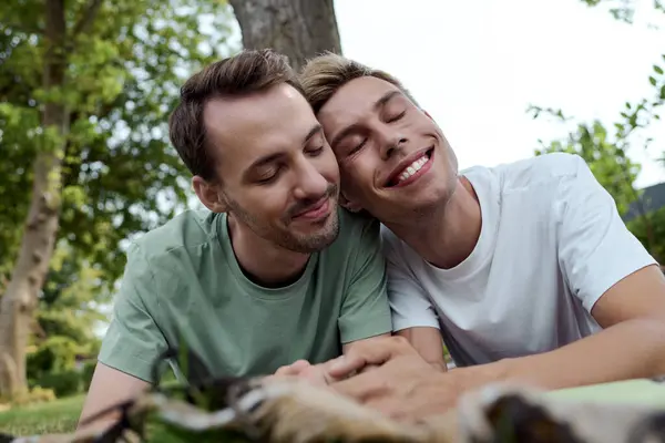 Deux hommes partagent un moment chaleureux, souriant et relaxant ensemble dans un parc ensoleillé. — Photo de stock