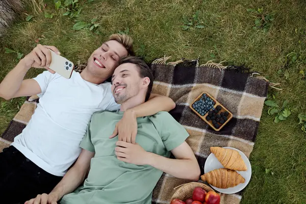 Two happy partners share a cozy picnic, laughing together and savoring delicious treats outdoors. — Stock Photo
