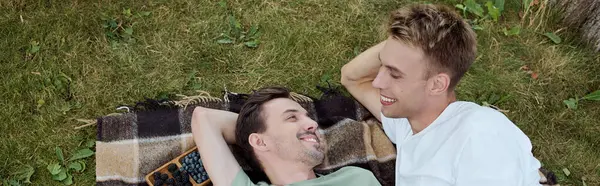 Two joyful men share a moment of connection while lying on a blanket in the grass. — Stock Photo