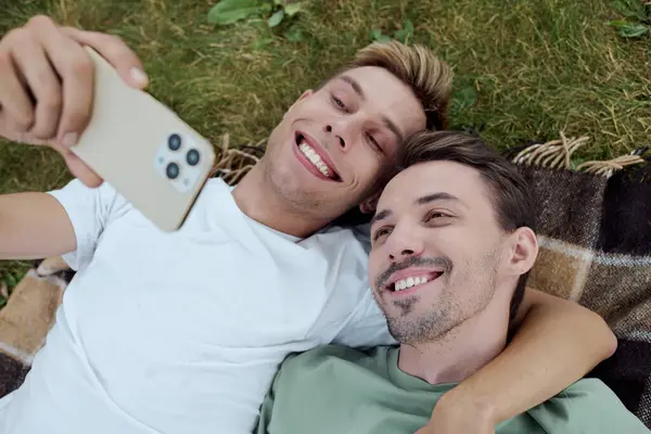 A handsome couple enjoys a sunny day, smiling while taking a selfie together on a blanket. — Stock Photo