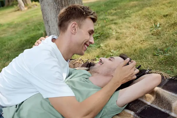 A happy couple shares a tender moment on a blanket, surrounded by lush greenery on a sunny day. — Stock Photo