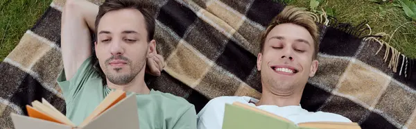A charming couple lies side by side on a cozy blanket, lost in their books under the sun. — Stock Photo