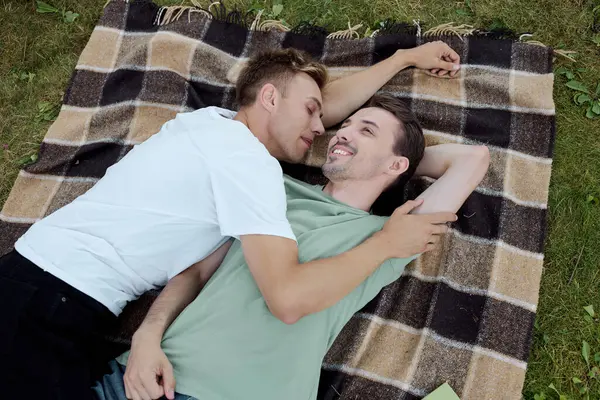 Two happy men share a loving embrace while lounging on a cozy blanket outdoors. — Stock Photo