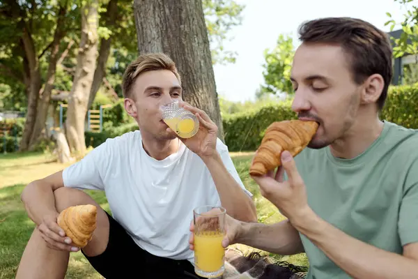 Due partner felici condividono un delizioso momento con croissant e succo rinfrescante all'aperto. — Foto stock