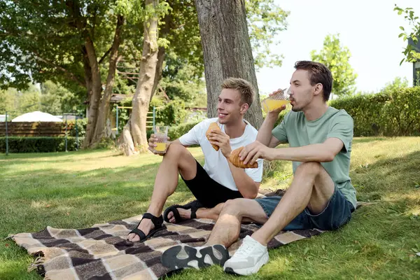 Two joyful friends relax on a blanket, sipping refreshing drinks and sharing moments together. — Stock Photo