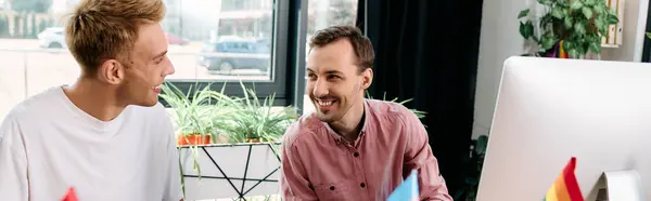 Two smiling men share a light hearted conversation while working together in a bright room. — Stock Photo