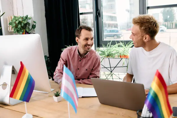 Two handsome men collaborate joyfully in a lively workspace adorned with pride flags. — Stock Photo