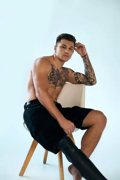 A young man with striking tattoos showcases his prosthetic leg while sitting in a modern studio. — Stock Photo