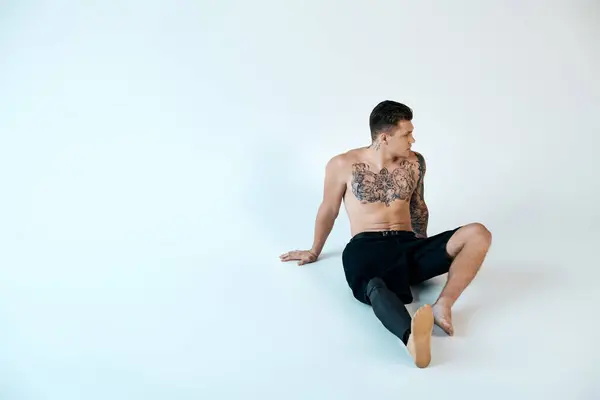 A young man with striking tattoos showcases his prosthetic leg while seated in a serene studio. — Stock Photo