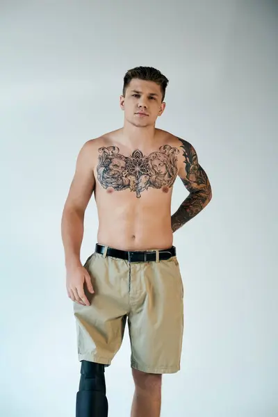 A confident young man with intricate tattoos showcases his prosthetic leg in a minimalist studio environment. — Stock Photo