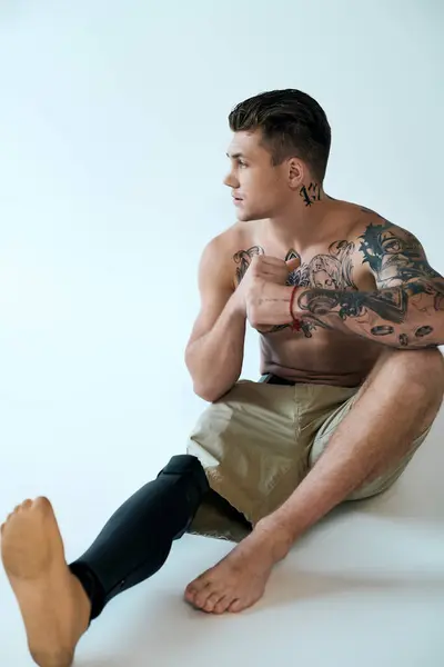 A tattooed young man sits in a studio, highlighting his determination and strength with a prosthetic leg. — Stock Photo