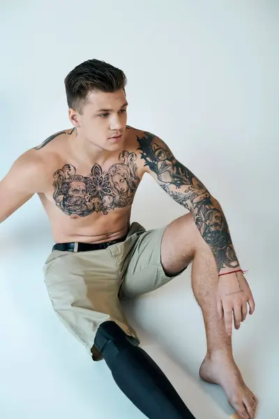 Um jovem tatuado mostra sua perna protética enquanto golpeia uma pose pensativa em um estúdio. — Fotografia de Stock
