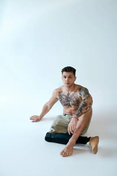 A tattooed young man sits gracefully in a studio, showcasing his prosthetic leg and strength with pride. — Stock Photo