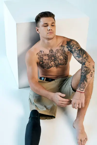 Ein tätowierter junger Mann mit Beinprothese sitzt elegant in einem modernen Studio und präsentiert seine Kunst. — Stockfoto