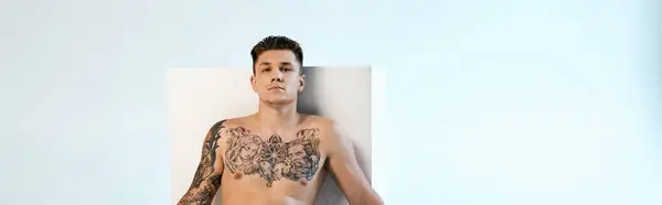 The young man displays intricate tattoos while seated in a bright studio. — Stock Photo
