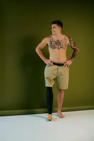 A young man with vibrant tattoos showcases his prosthetic leg while posing in a studio filled with creativity. — Stock Photo