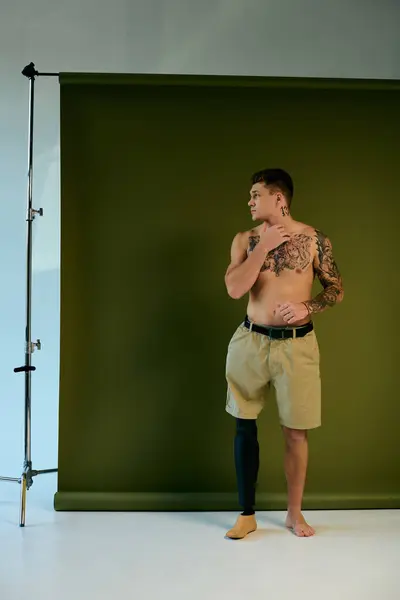 Um jovem tatuado está com uma perna protética, mostrando sua arte corporal em um ambiente de estúdio criativo. — Fotografia de Stock