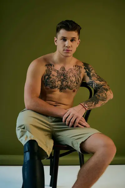 A young man with striking tattoos sits gracefully in a studio, showcasing his prosthetic leg and strength. — Stock Photo