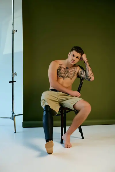 A tattooed young man showcases his prosthetic leg while sitting gracefully in a studio environment. — Stock Photo