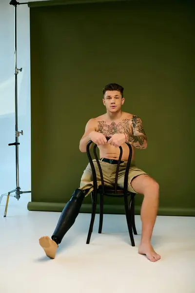 Un jeune homme tatoué s'assoit sur une chaise, présentant sa jambe prothétique et son expression artistique dans un studio. — Photo de stock