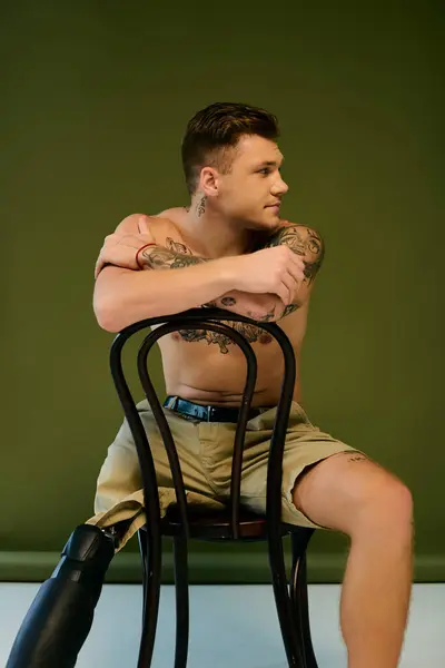A tattooed young man sits on a chair, showcasing his prosthetic leg while embracing his unique style. — Stock Photo