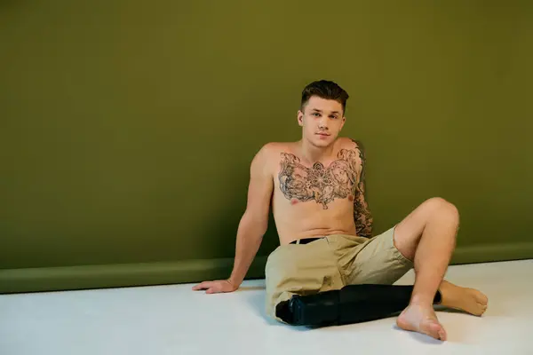Ein junger Mann mit aufwändigen Tätowierungen sitzt auf dem Boden und präsentiert seine Beinprothese vor einer stilvollen Kulisse. — Stockfoto