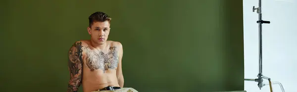 A young man showcasing intricate tattoos and sits elegantly in a studio setting. — Stock Photo