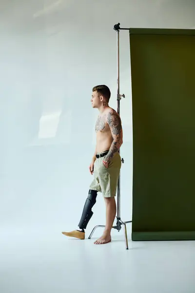 A confident young man with tattoos stands stylishly with a prosthetic leg in a contemporary studio — Stock Photo