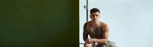 A tattooed young man sits confidently in a studio, showcasing his prosthetic leg and artistic expression. — Stock Photo