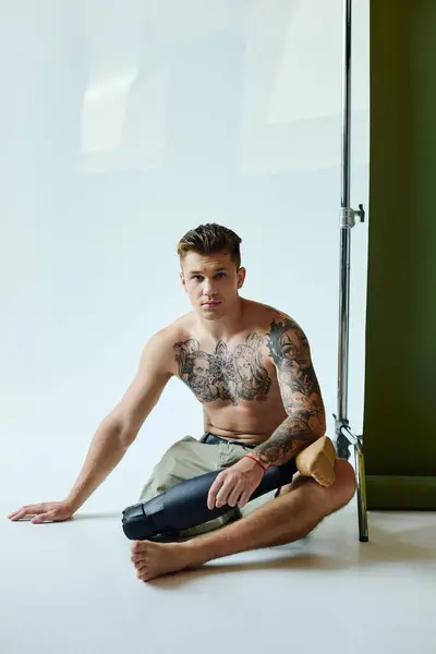 Dans un studio lumineux, un jeune homme tatoué confiant avec une jambe prothétique met en valeur sa force et son individualité. — Photo de stock