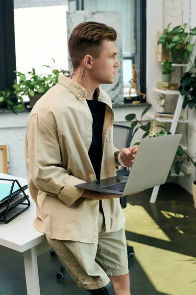 A focused young man balances his laptop while seated, showcasing his determination in a stylish workspace. — Stock Photo