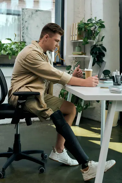 A skilled young professional with a prosthetic leg engages with a laptop while enjoying coffee. — Stock Photo