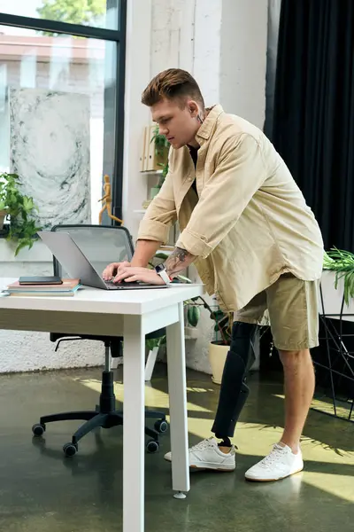 A determined young man with a prosthetic leg engages with his laptop in a stylish office space. — Stock Photo