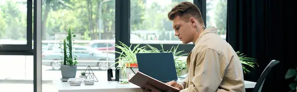 Un joven guapo se sienta en su escritorio, inmerso en la lectura - foto de stock
