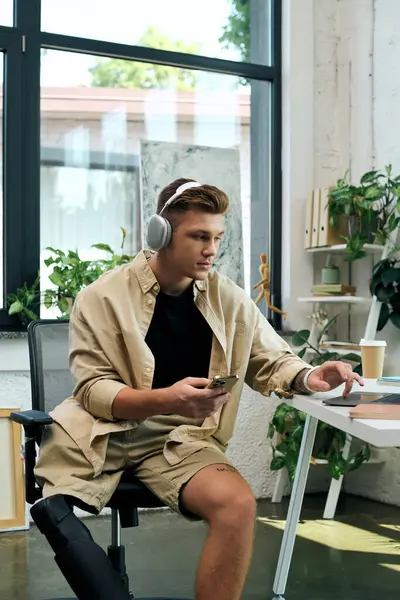 In a bright office, a handsome young man with a prosthetic leg engages with his smartphone while working. — Stock Photo