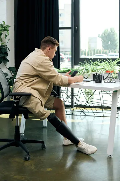 A young man with a prosthetic leg diligently writes at his desk in a chic office, showcasing his commitment. — Stock Photo