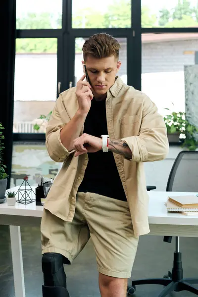 A determined young man with a prosthetic leg checks his watch while making a phone call at work. — Stock Photo