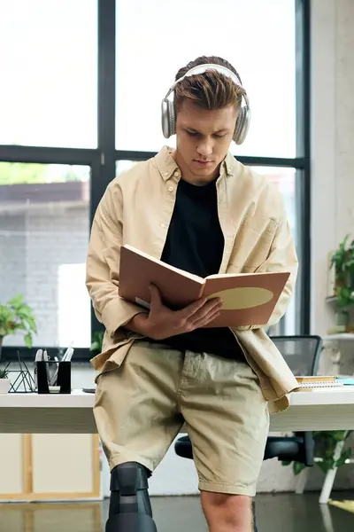 A young man with a prosthetic leg enjoys reading while working in a stylish office setting. — Stock Photo