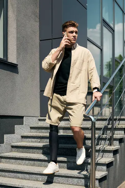 Un joven camina con confianza por las escaleras de una oficina moderna mientras habla por teléfono. - foto de stock