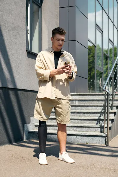 Handsome young man wearing casual attire checks his smartphone while standing by an office entrance. — Stock Photo