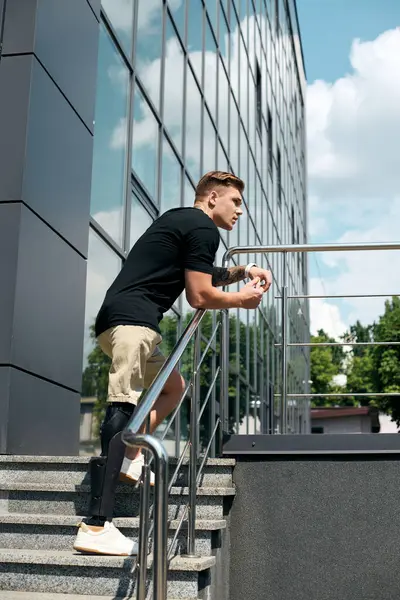 Um jovem profissional com uma perna protética se inclina contra um corrimão, contemplando sua jornada de trabalho no escritório. — Fotografia de Stock