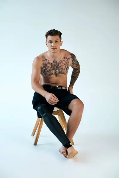 Un jeune homme tatoué pose sur un tabouret dans un studio, présentant sa prothèse de jambe et son art corporel. — Photo de stock