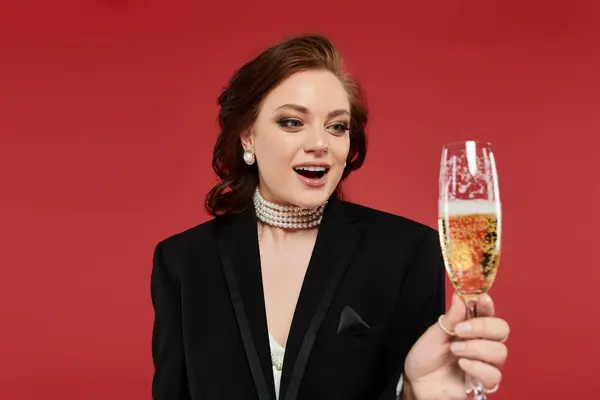 A joyful young woman in a sophisticated outfit raises a champagne glass, celebrating an occasion. — Stock Photo
