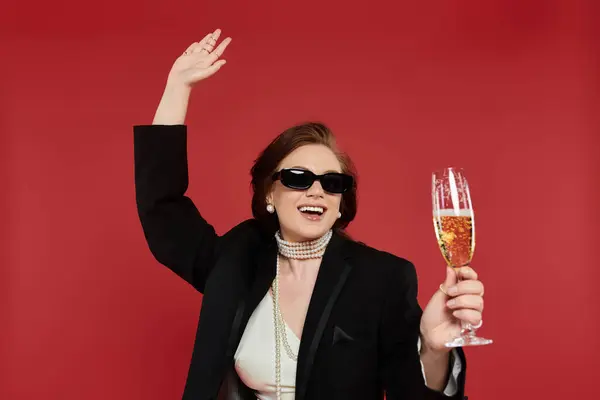 A stylish young woman joyfully raises a glass against a bright backdrop. — Stock Photo