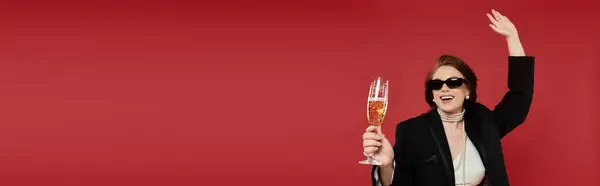 A young woman in elegant attire joyfully raises a champagne glass, celebrating in a vibrant setting. — Stock Photo