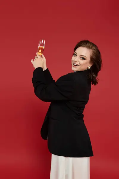 The young woman in elegant attire joyfully raises her glass with a smile. — Stock Photo